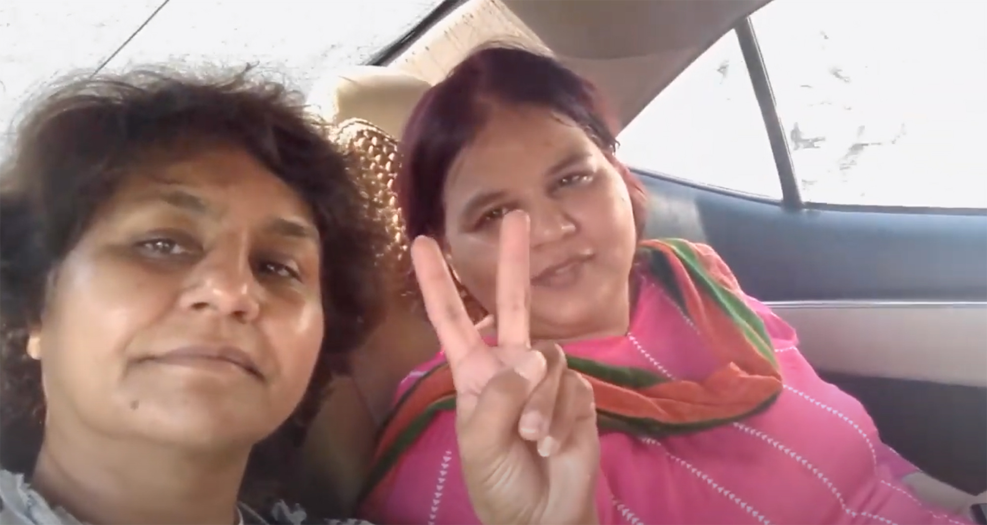 Two women in car. One making the peace-sign with her hand.